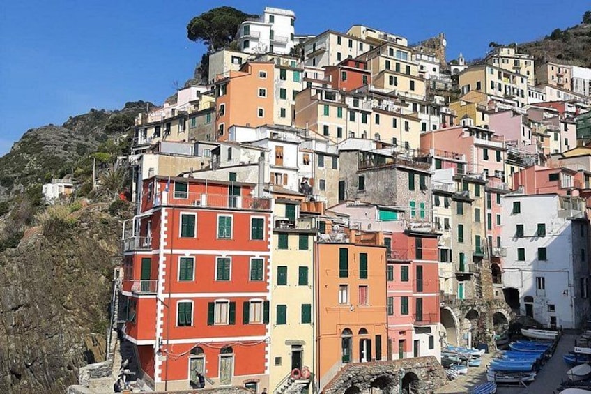 Una ladera densamente poblada con edificios coloridos, cielo despejado y un estrecho canal con barcos. 1