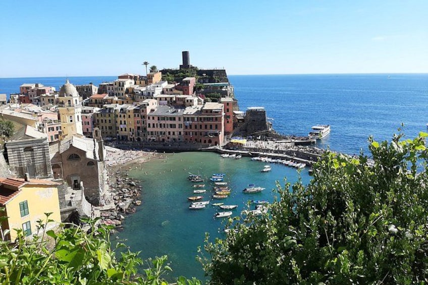 Un pueblo costero con edificios históricos, un puerto con barcos y un mar azul cristalino. 2
