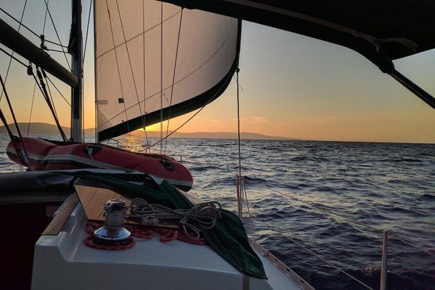 Un velero al atardecer con un mar tranquilo, un horizonte con tierra a lo lejos y un salvavidas en la cubierta. 2