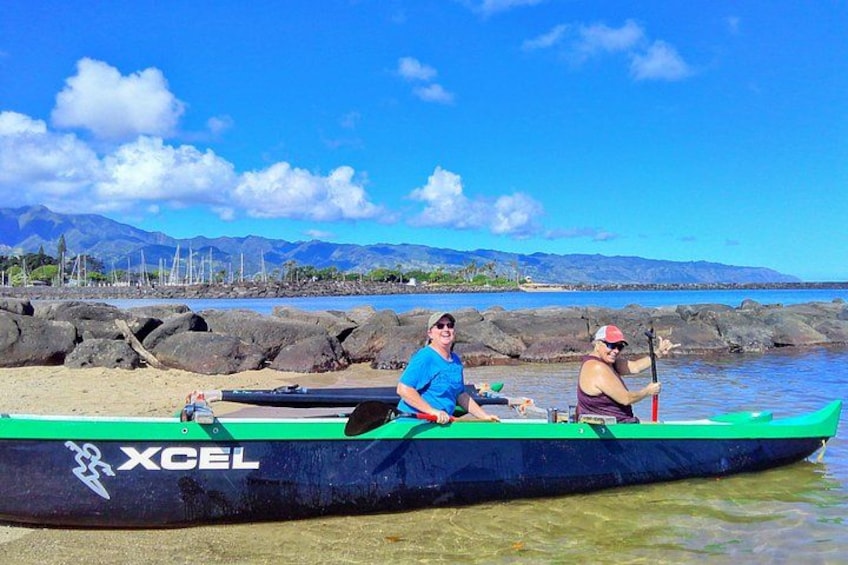 Two people in a green kayak on a beach with a clear sky and mountains in the background. 3