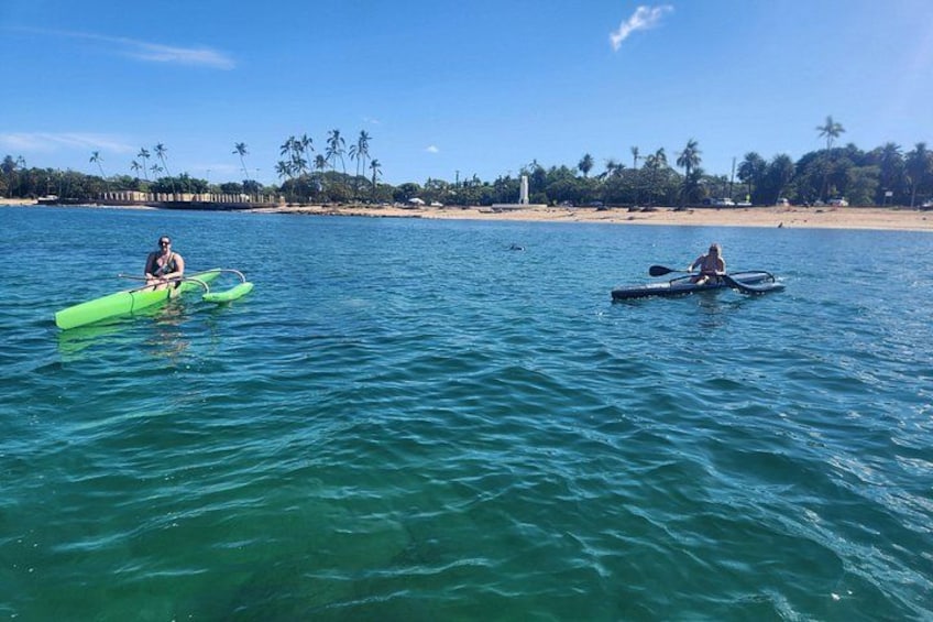 Two people kayaking on a calm sea with a beach and palm trees in the background. 5