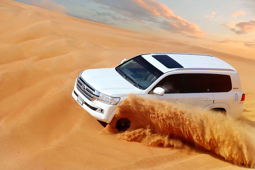 A white SUV driving through a desert with sand dunes. 1