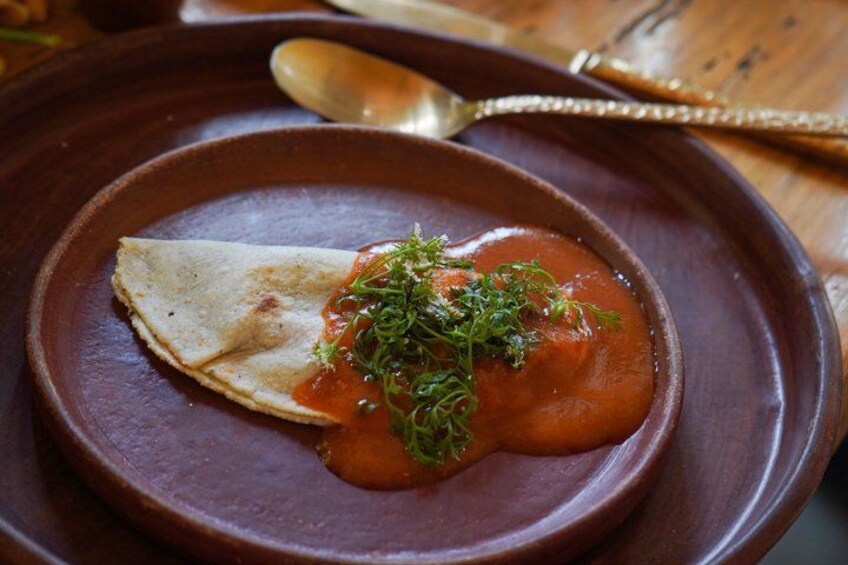 Une assiette contenant une crêpe pliée et une sauce à base de tomates, le tout garni d’herbes aromatiques. 4