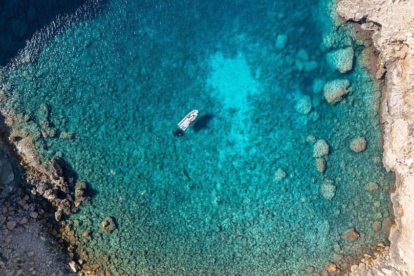 A boat anchored in clear turquoise waters with rocky formations on the shore. 2