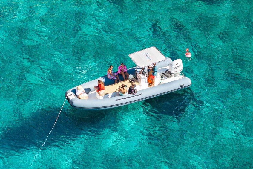 A small inflatable boat with people on board, floating on clear turquoise water. 1