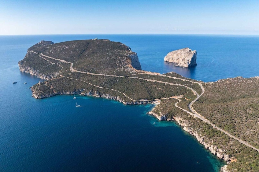 An aerial view of a coastal landscape with a prominent rocky outcrop, a winding road, and clear blue waters. 4