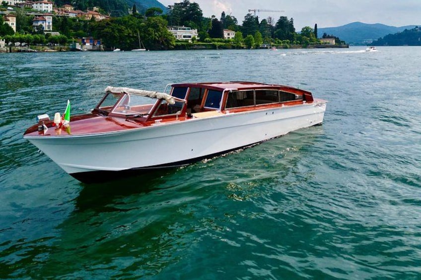 Un velero blanco con cabina roja sobre aguas tranquilas, rodeado por un lago con casas y árboles al fondo. 5