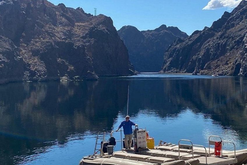 A calm lake surrounded by rocky cliffs, a boat docked at the shore, and a person standing on the dock. 5