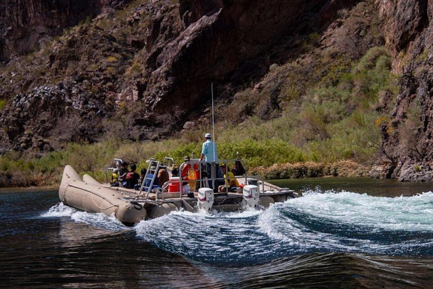 A raft boat navigating a river with a rocky canyon in the background. 3