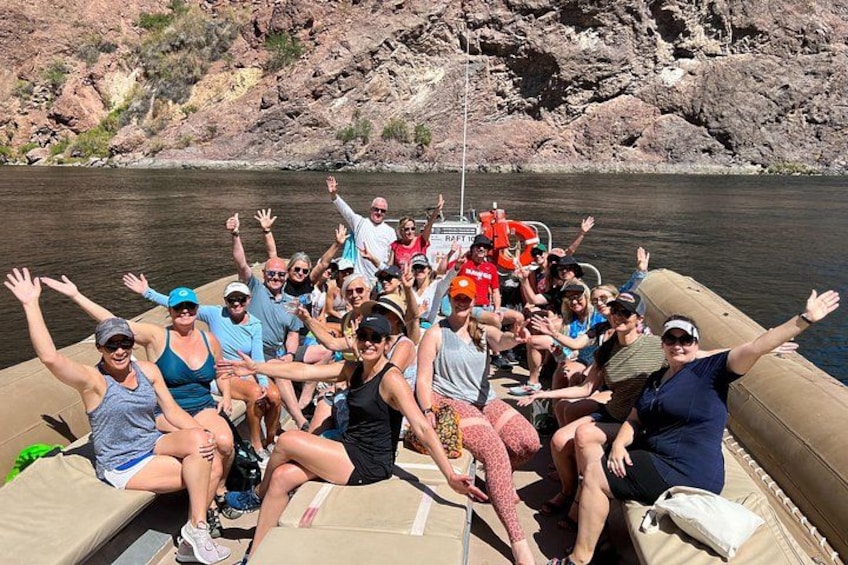 A group of people on a boat with their arms raised, surrounded by a rocky landscape and water. 2