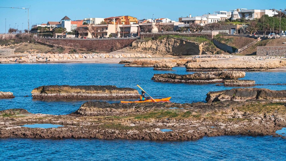 A kayaker on a rocky shoreline with buildings in the background. 2