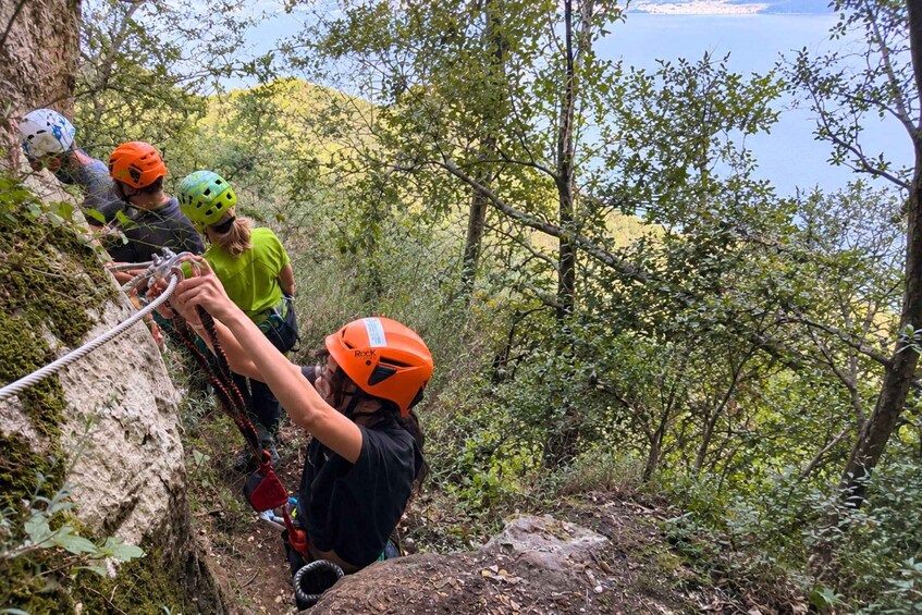 Un grupo de personas haciendo rappel por un acantilado rocoso, con un área boscosa y un cuerpo de agua al fondo. 3