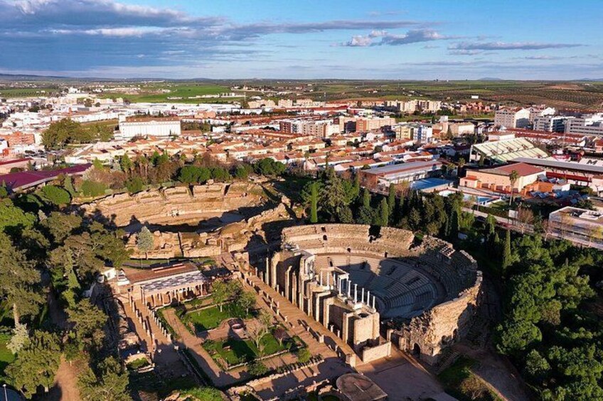 An ancient amphitheater surrounded by modern buildings and greenery. 3