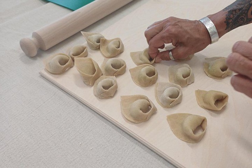 En person laver dumplings på en træplade, en kagerulle ligger i nærheden. 3