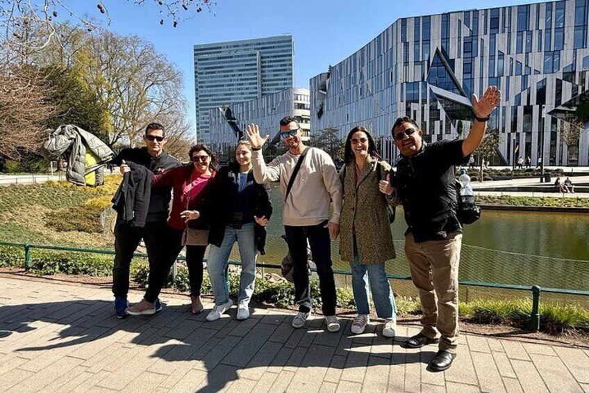 A group of people standing by a water body with a modern building in the background. 1