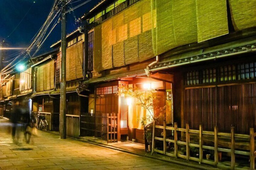 A traditional Japanese street at night with illuminated buildings and a person riding a bicycle. 2