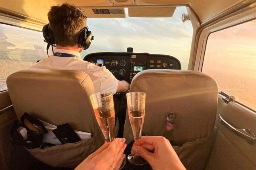 A pilot at the controls of an aircraft with passengers holding champagne glasses. 1