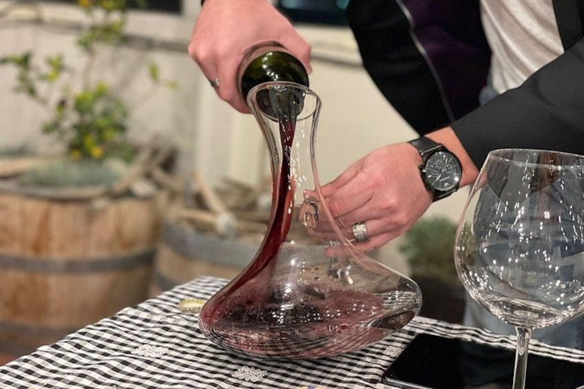 A person pouring red wine from a glass decanter into a wine glass. 5
