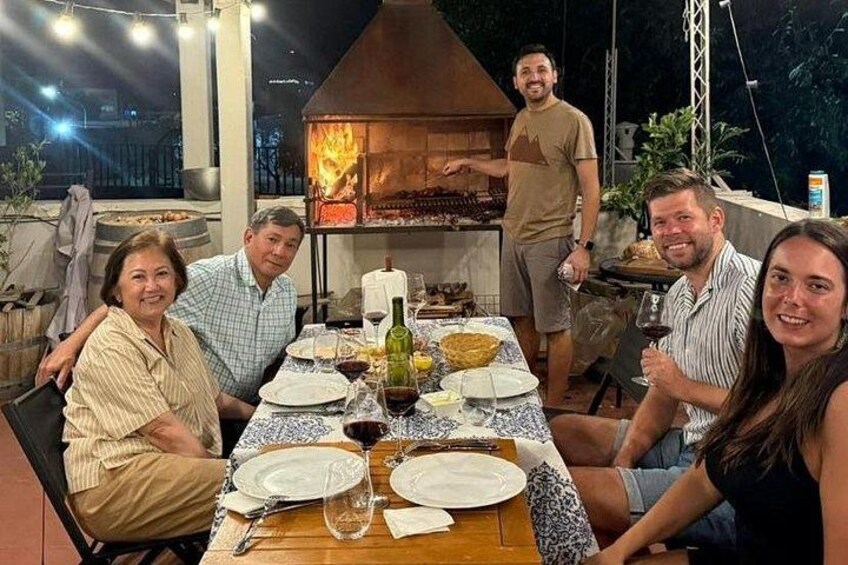 A group of people dining outdoors at night with a wood-fired oven in the background. 2
