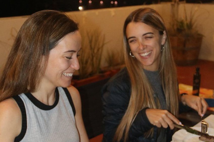 Two people sitting at a table with a bottle and a plate of food. 3