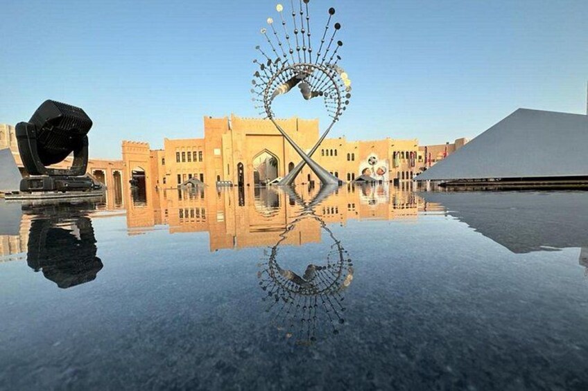 A reflective water surface with a geometric sculpture and traditional architecture in the background. 3