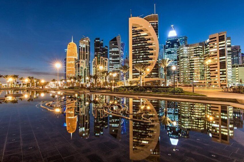 Horizonte urbano al anochecer con edificios modernos, una estructura grande y reflectante, y una masa de agua tranquila que refleja las luces. 5