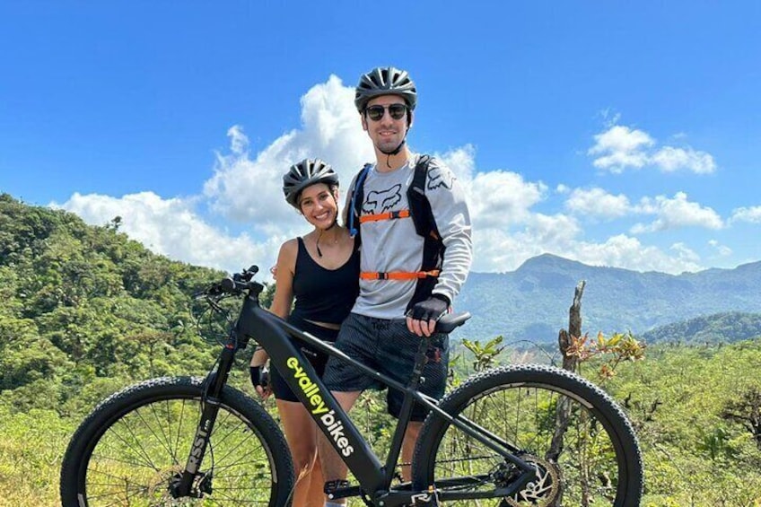 Two people on a mountain bike trail with a scenic mountain backdrop. 1