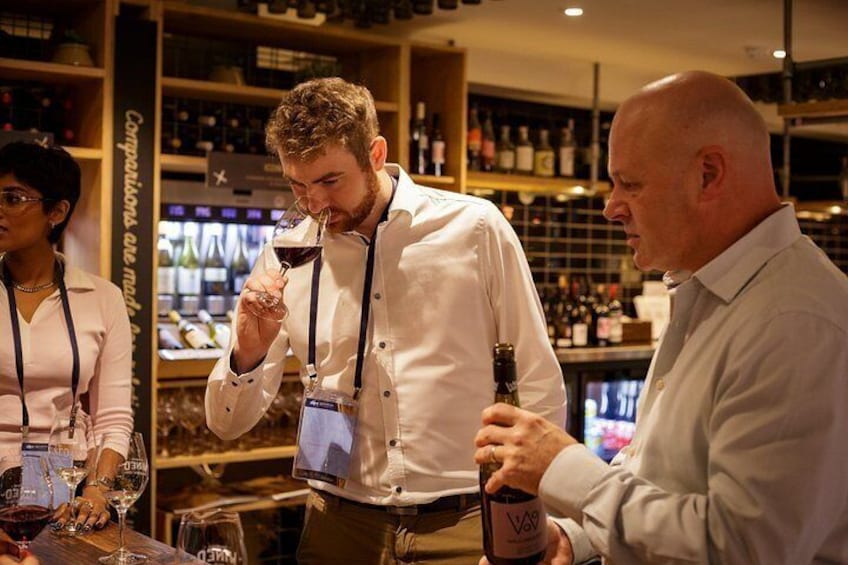 A person holding a wine glass and a bottle, standing in a bar with shelves of bottles in the background. 3