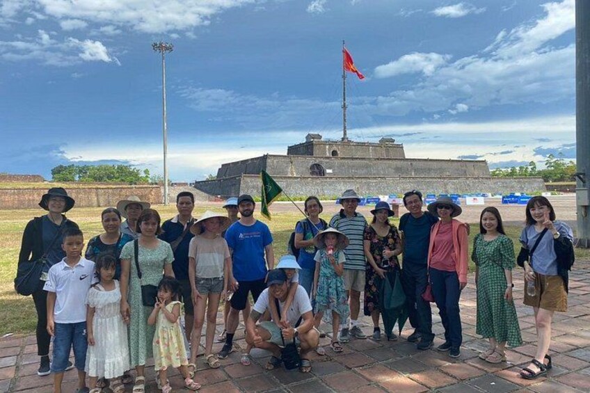 A group of people posing in front of a historical fort with a flag on top. 3