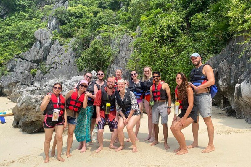 A group of people on a sandy beach with rocky cliffs and greenery in the background. 2