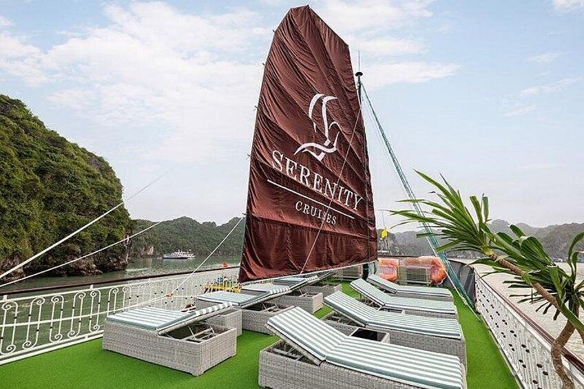 A sailboat with a large brown sail, surrounded by a green deck and white railings, with a mountainous landscape in the background. 3