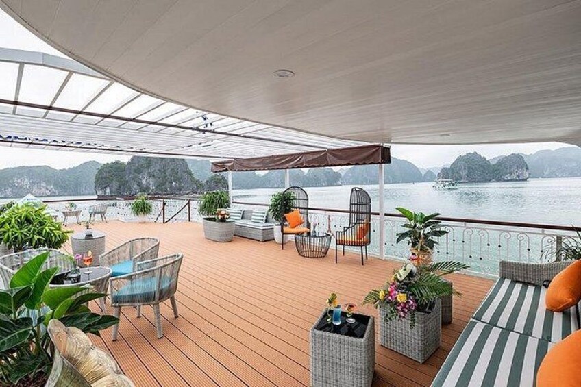 A covered outdoor deck with seating and potted plants, overlooking a body of water and hills. 5