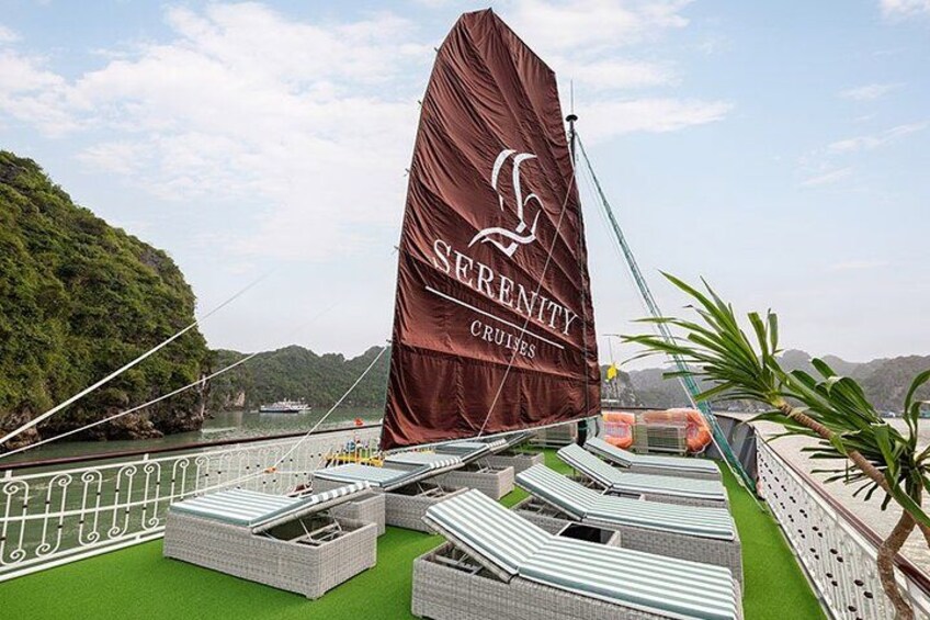 A sailboat with a large brown sail, named 'Serenity Cruises,' docked at a port with green decking and a mountainous backdrop. 5