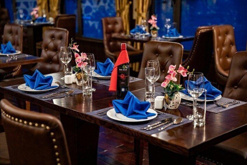 A formal dining table set with blue napkins, wine glasses, and a bottle of red wine. 3