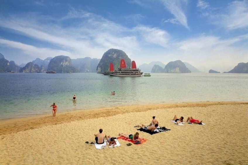 A beach with people sunbathing, a boat with red sails, and distant mountains. 2