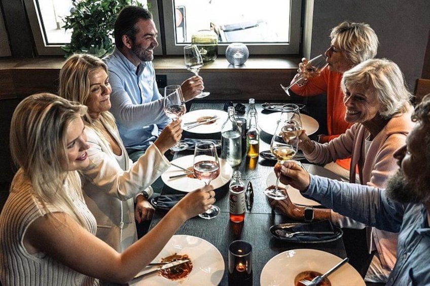 A group of people sitting around a table, toasting with wine glasses. 1