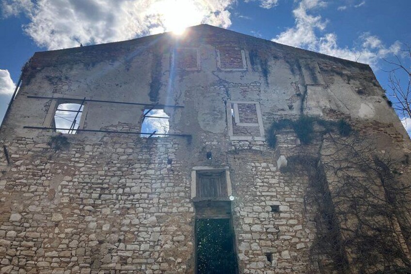 A weathered stone building with a partially intact roof, a visible window, and a door. 4