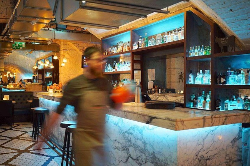 A bar with marble countertops, shelves of bottles, and stools. 2