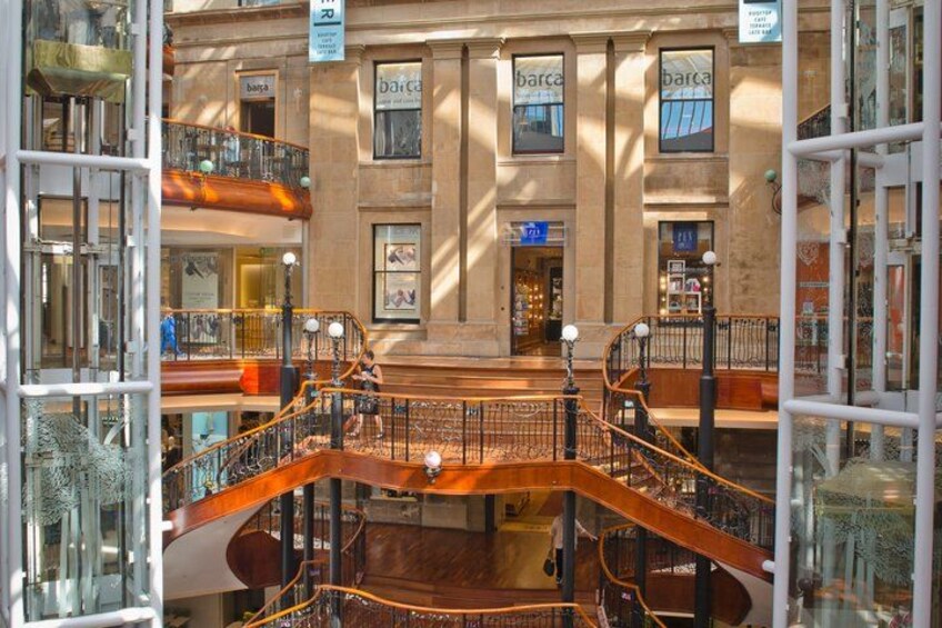 A multi-level atrium with glass railings, a central staircase, and multiple 'barca' signs. 2