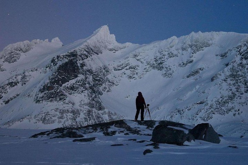 Eine Person steht mit einem Stativ auf einem schneebedeckten Berggipfel. 5
