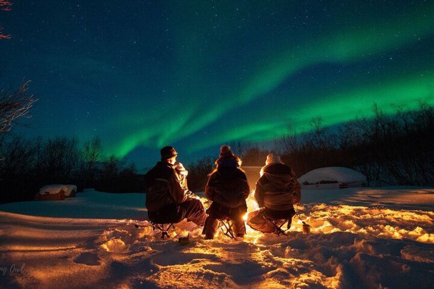 Drei Personen sitzen im Schnee und beobachten das Nordlicht. 1