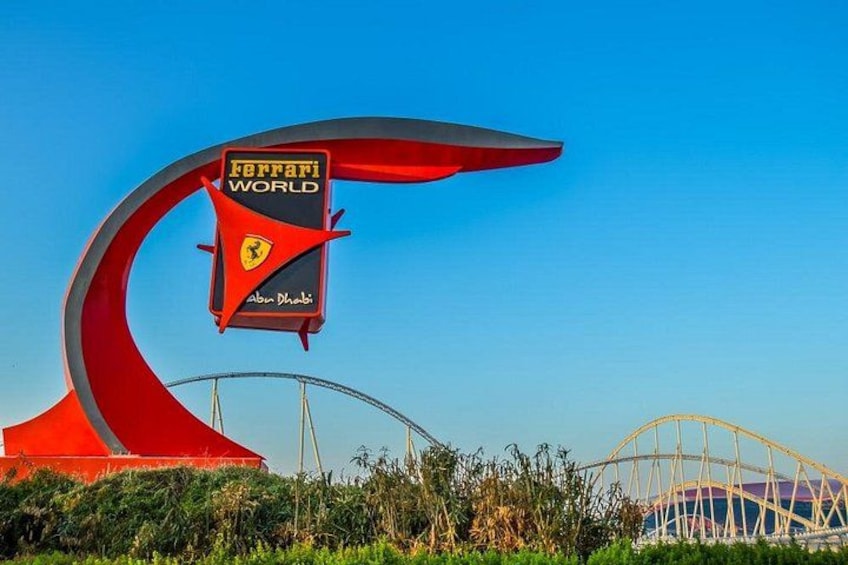 A Ferrari World sign with a red arch structure, a clear blue sky, and a roller coaster in the background. 2