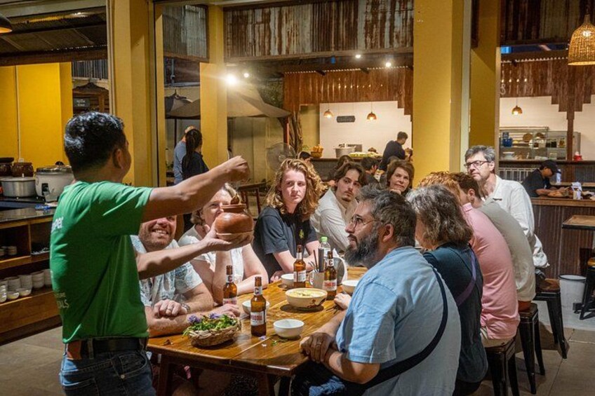 Un groupe de personnes est réuni dans un restaurant dont l’intérieur est en bois et dont l’ambiance est décontractée. 1