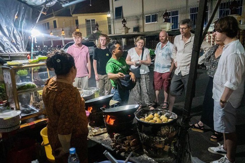 Un groupe de personnes se trouve autour d’un espace dédié à la cuisine, où l’on peut voir des casseroles et un barbecue. 2