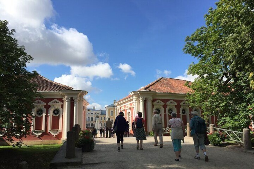 A group of people walking on a pathway between classical buildings with red and white facades. 1