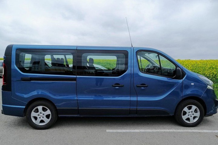 A blue van parked on a road with a field in the background. 2