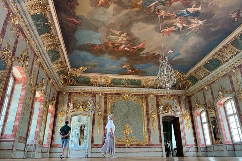 An opulent room with ornate gold detailing, a large chandelier, and a frescoed ceiling. 1