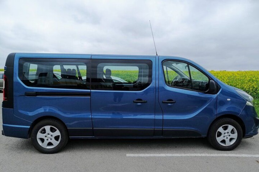 A blue van parked on a road with a field in the background. 2