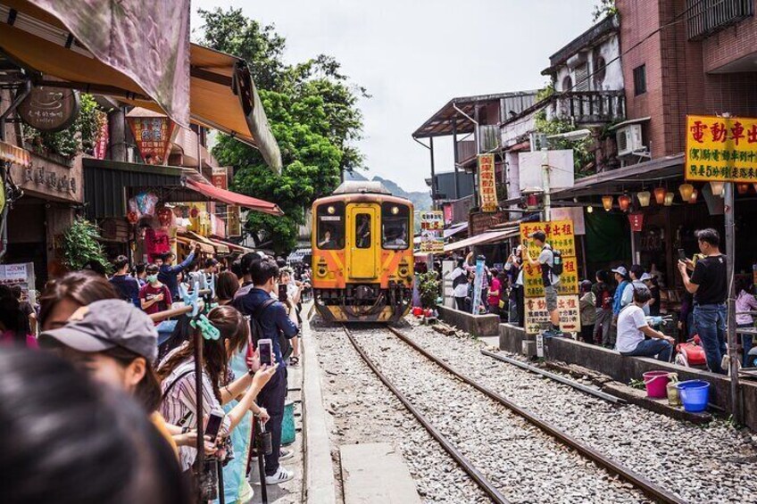 A train passing through a crowded street with people standing on the sides. 2