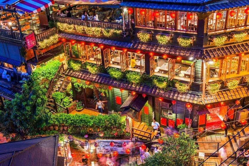 Un edificio tradizionale a più livelli con balconi, lanterne rosse e vegetazione. 1